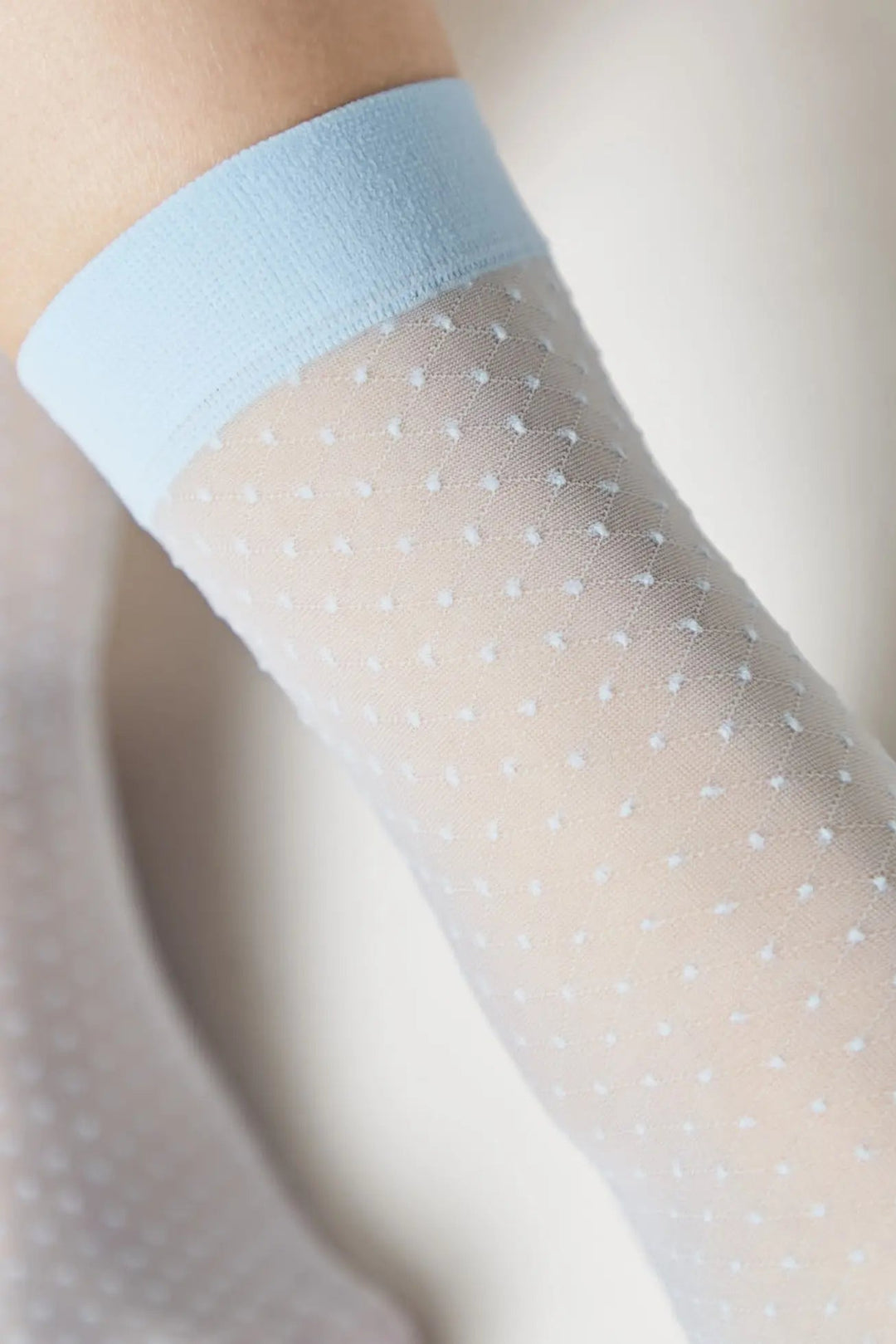 Sheer polka dot stockings with light blue top on a neutral background #color_light-blue