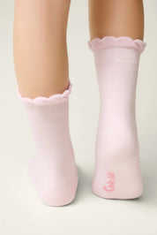 Pink socks with ruffled top worn by a person on a light gray background #color_light-pink