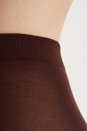 Close-up of a ribbed brown waistband, likely on a skirt or waistband garment, shown against a model's skin and a light neutral background.