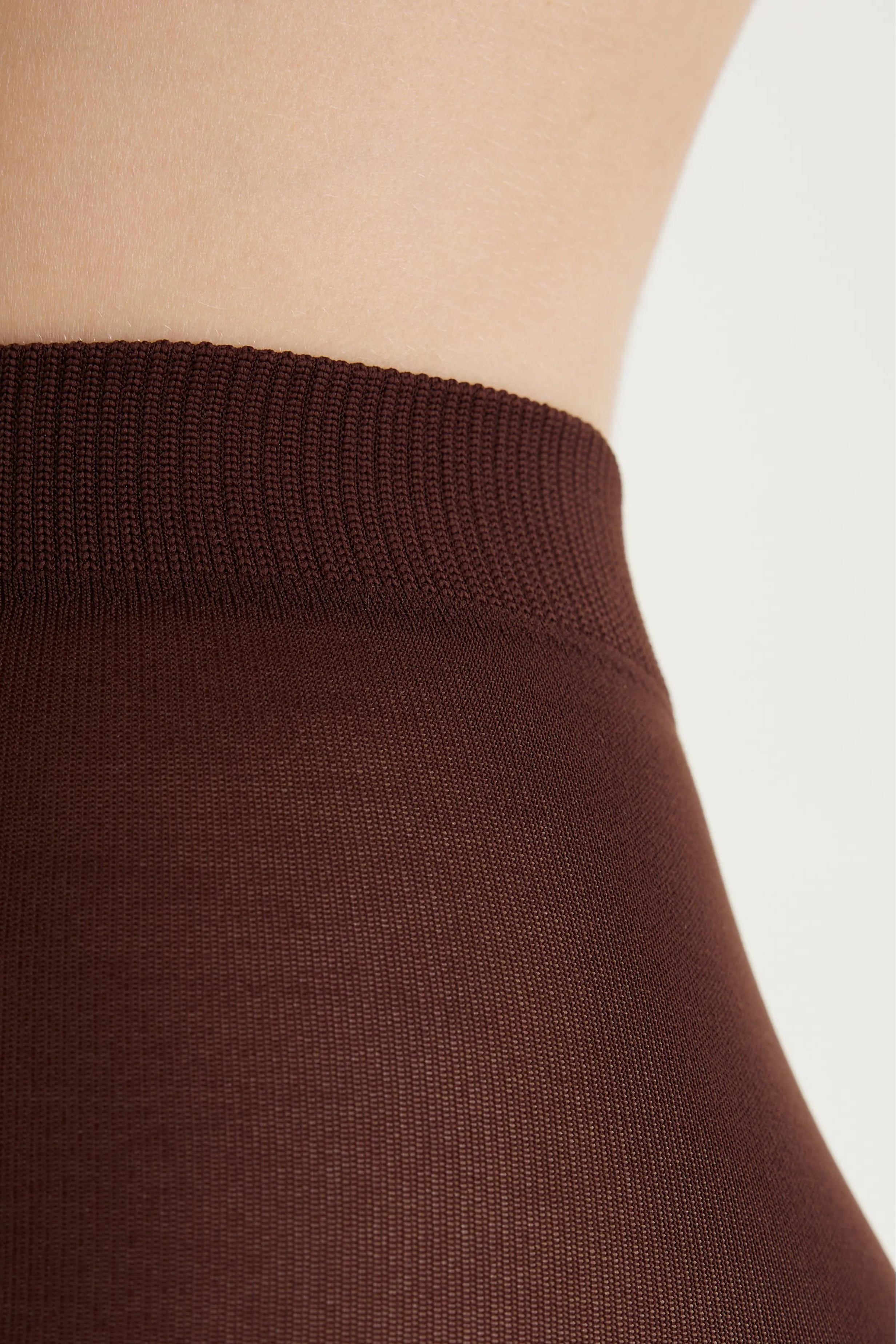 Close-up of a ribbed brown waistband, likely on a skirt or waistband garment, shown against a model's skin and a light neutral background.