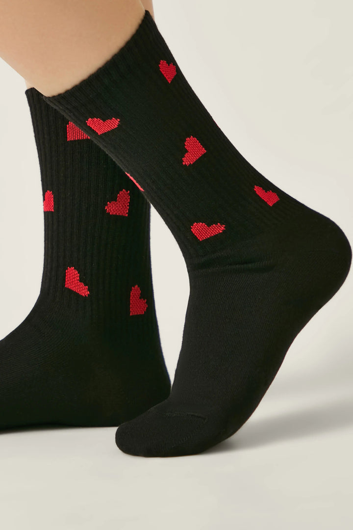 Black socks with red heart patterns worn by a person on a light gray background #color_black