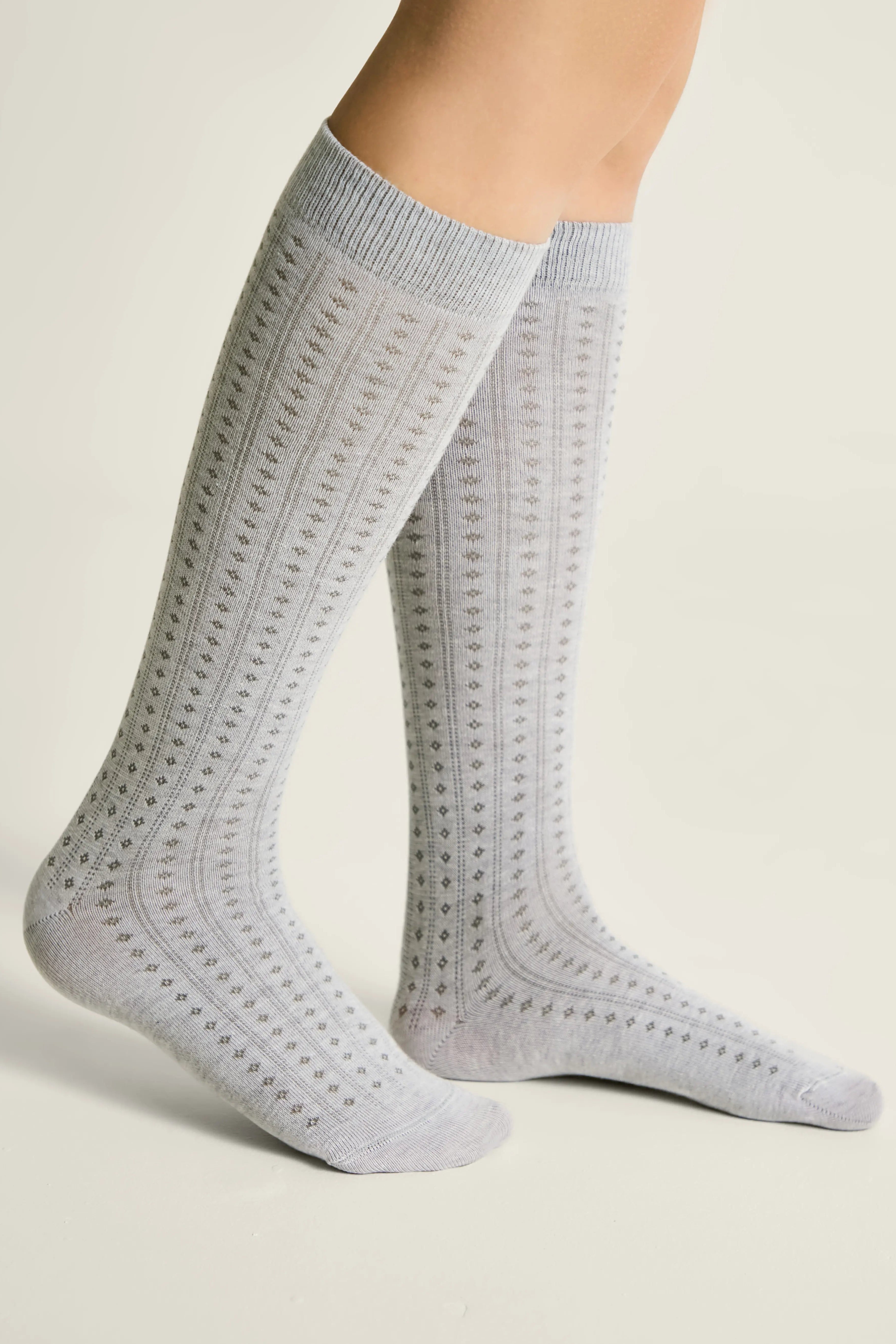 Gray knee-high socks with a subtle pattern worn by a person on a light background #color_light-gray