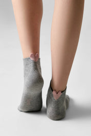 A pair of low-cut gray socks with a small pink heart detail at the back of the ankle, shown on a model's feet against a light gray background.