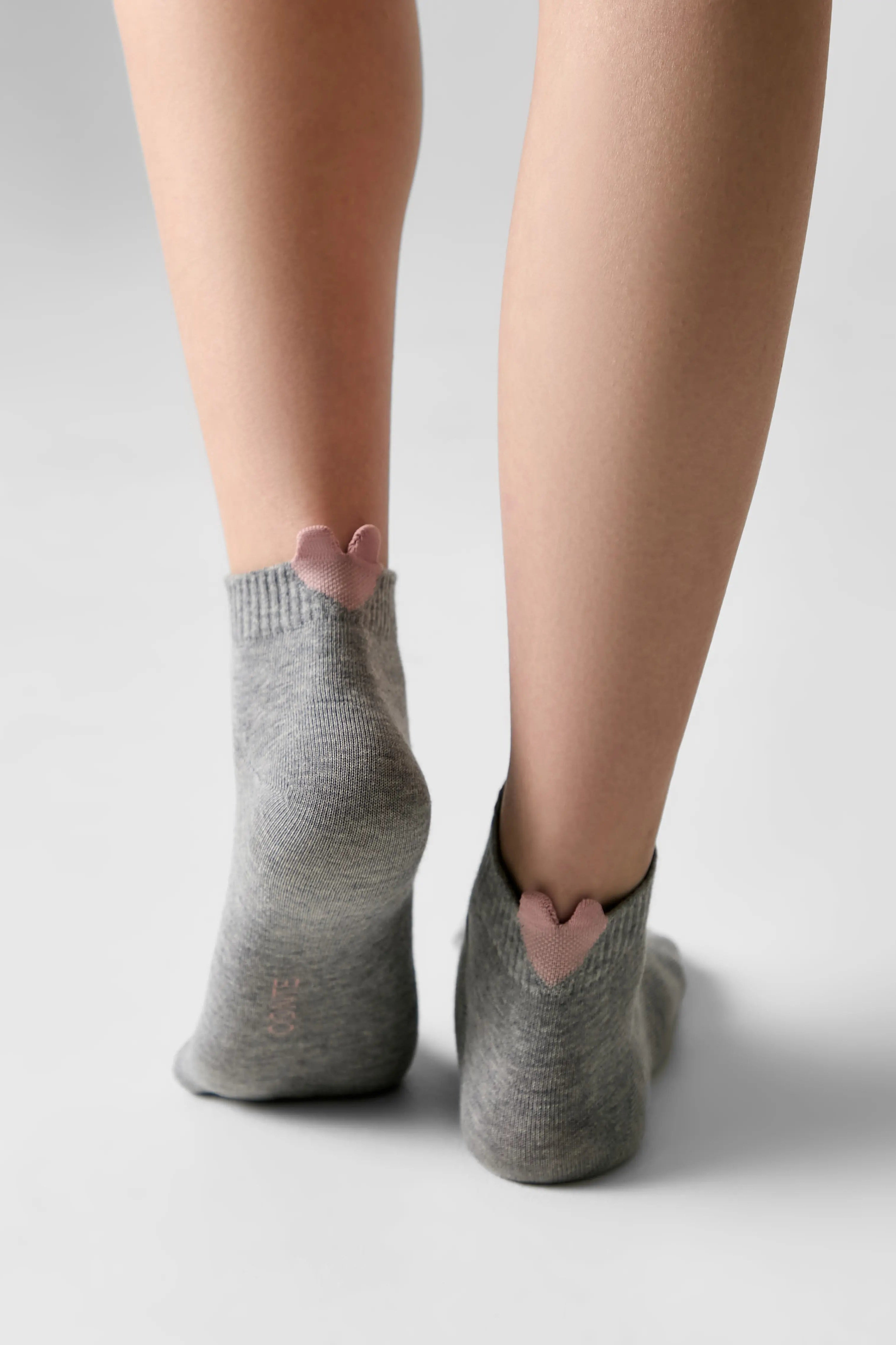 A pair of low-cut gray socks with a small pink heart detail at the back of the ankle, shown on a model's feet against a light gray background.