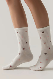White socks with heart patterns worn by a person on a light gray background #color_milky