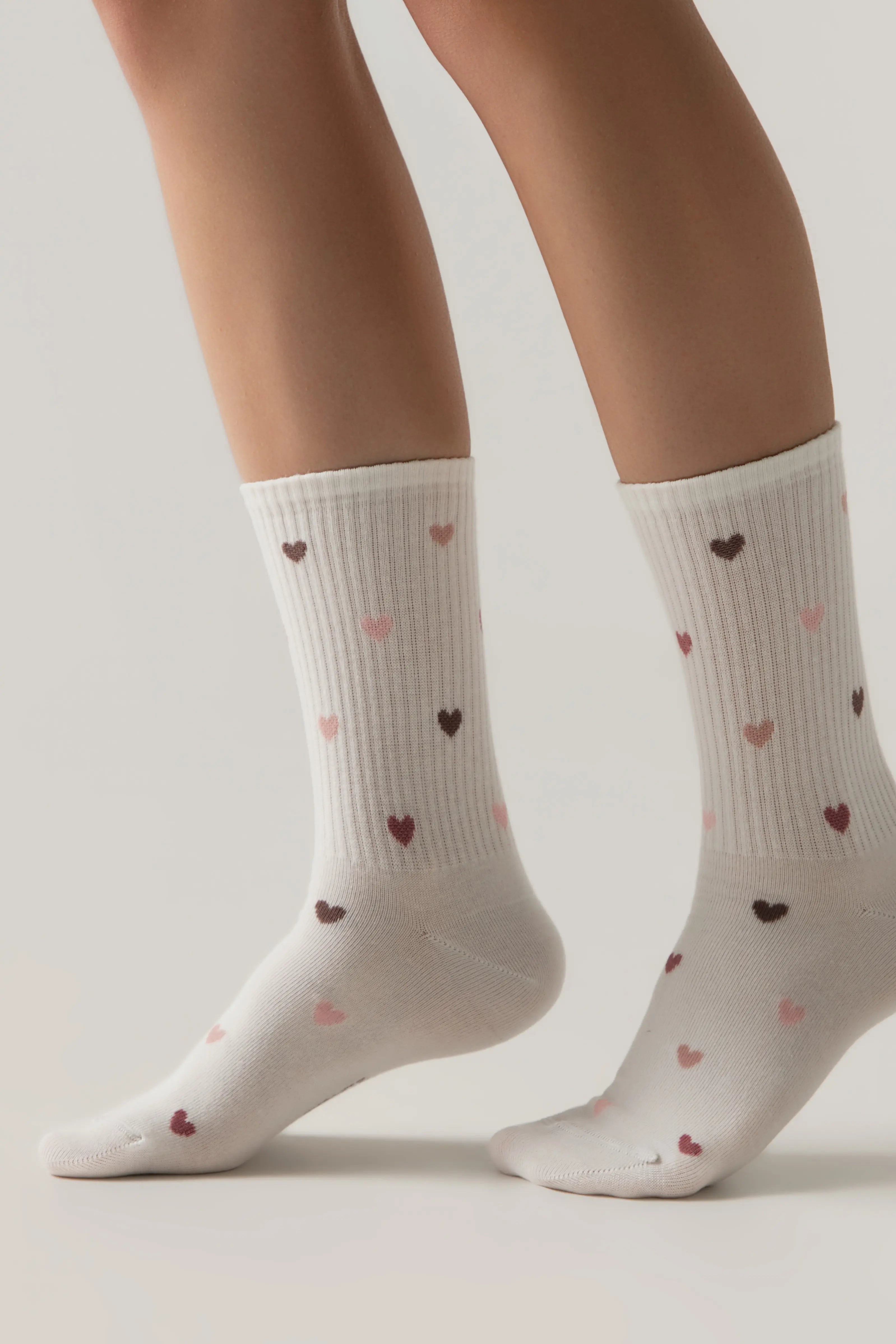 White socks with heart patterns worn by a person on a light gray background #color_milky