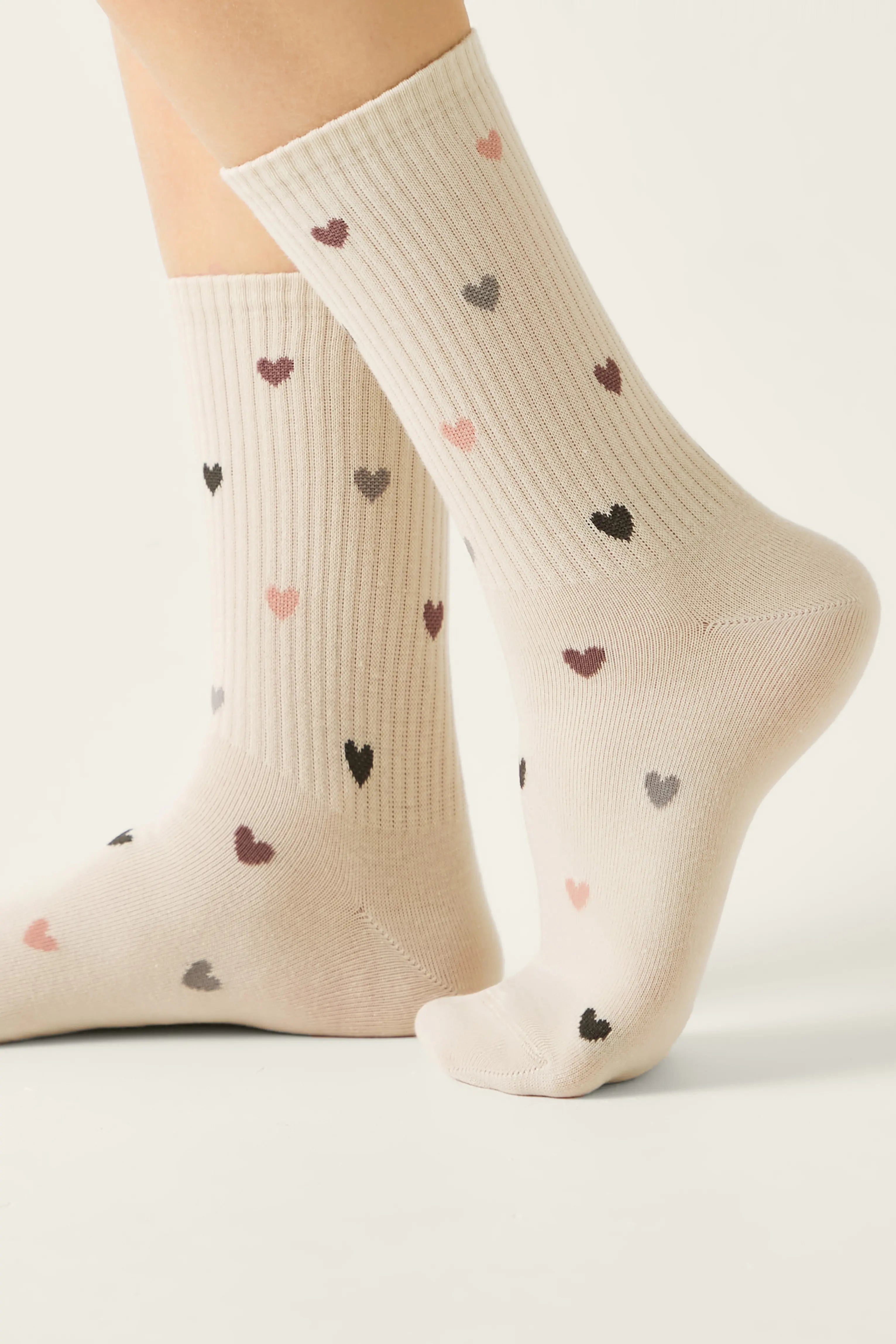 Beige socks with heart patterns worn by a person on a light background #color_beige