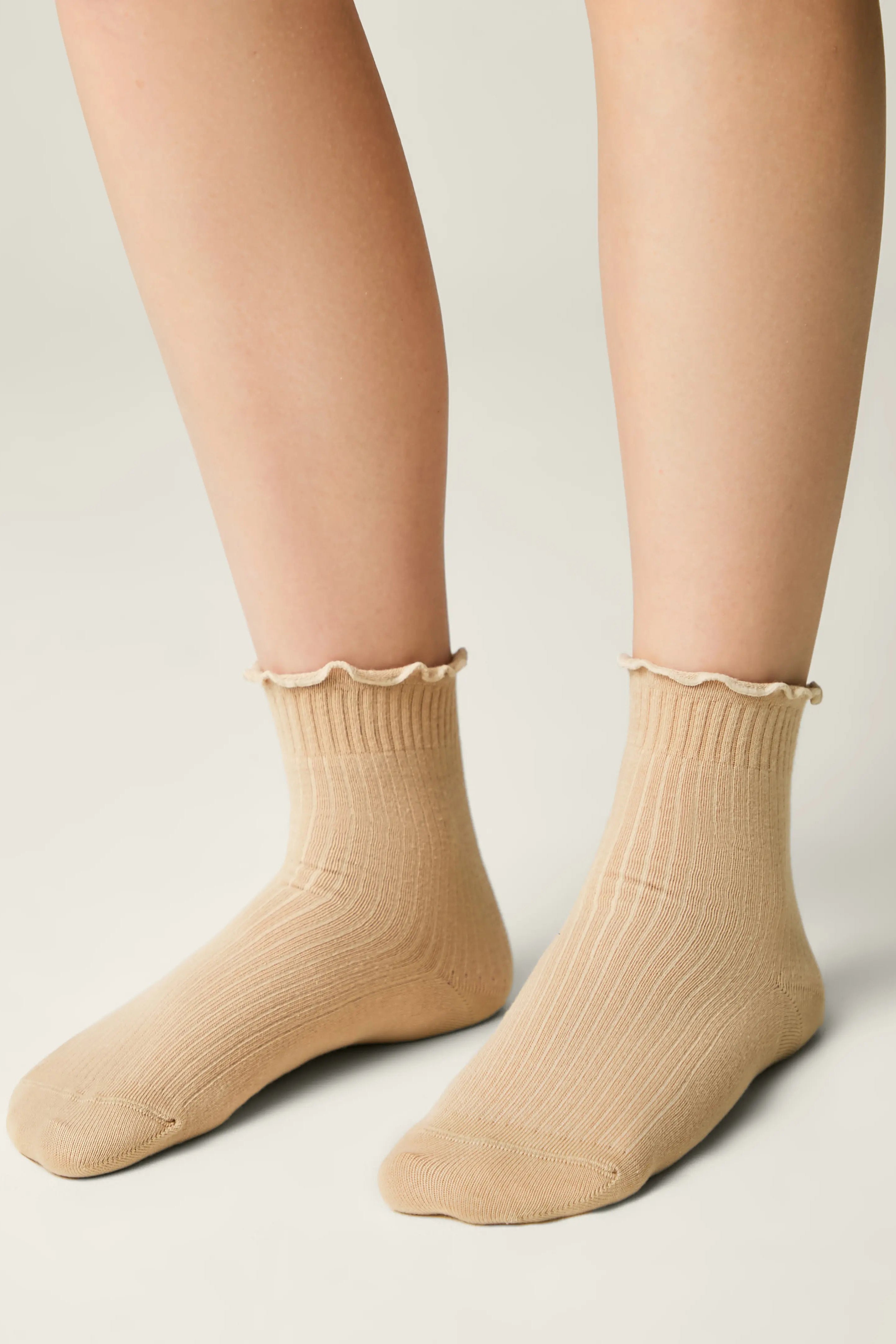 Beige socks with ruffled top worn by a person on a light gray background #color_beige