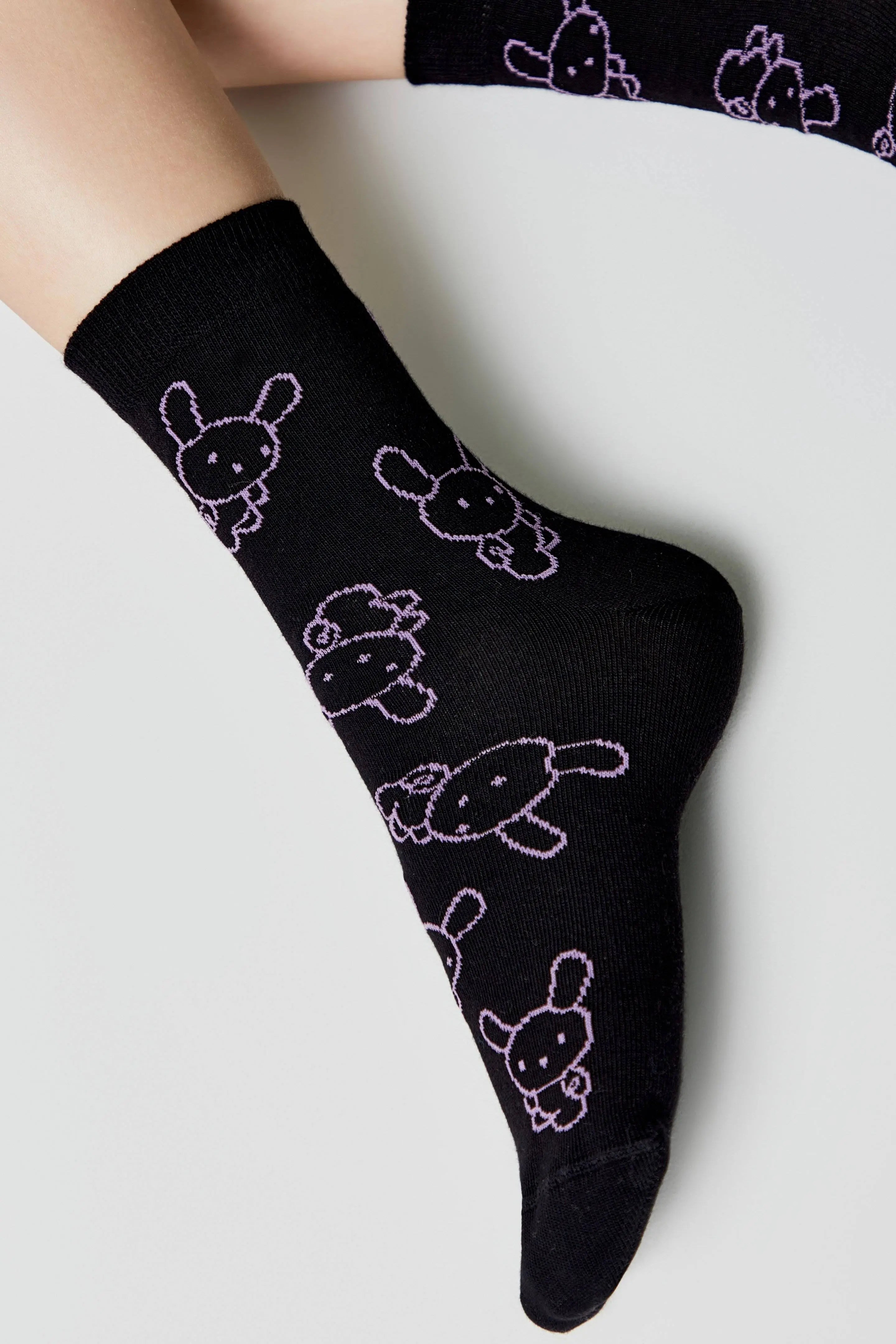 Black socks with white bunny designs worn by a person on a light gray background