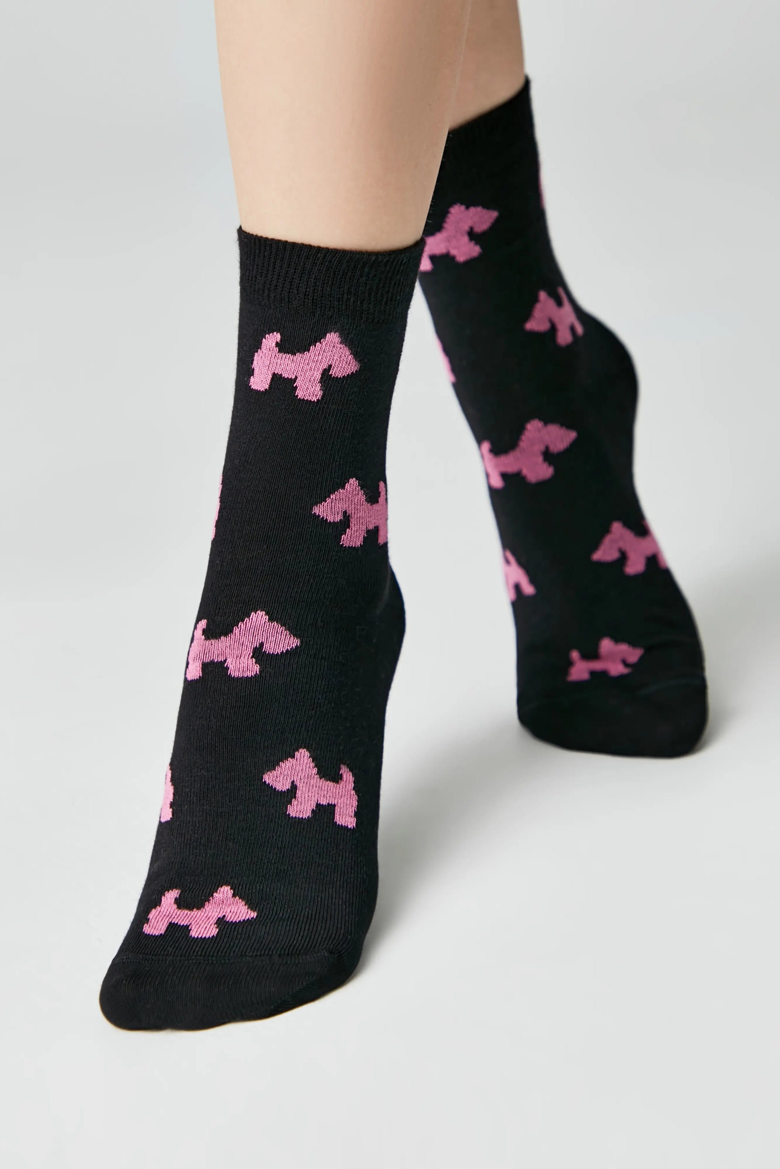 Black socks with pink dog patterns worn by a person on a light gray background #color_black