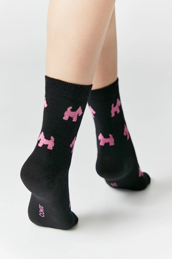 Black socks with pink dog patterns worn by a person on a light gray background #color_black