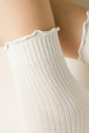 Close-up of a person wearing a white ribbed tank top with a blurred  background #color_milky