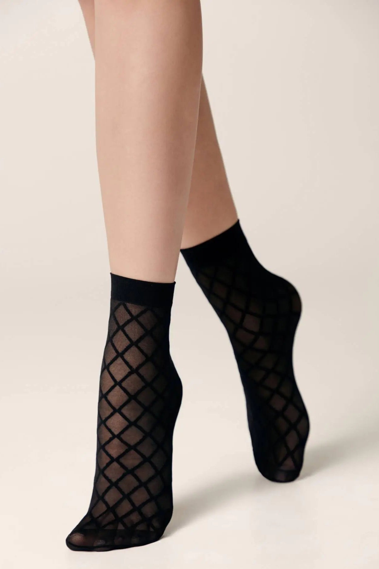 Black fishnet socks worn by a person on a beige background #color_nero-black