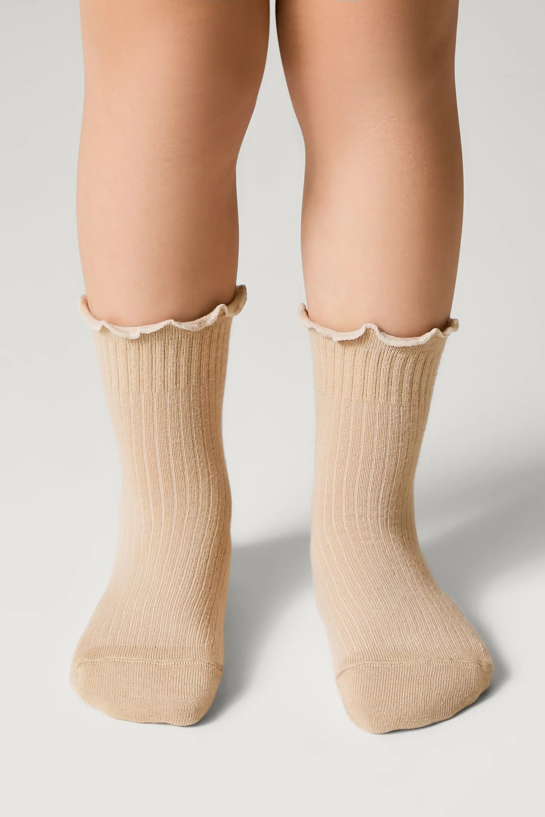Beige socks with ruffled top worn by a person on a light gray background #color_beige