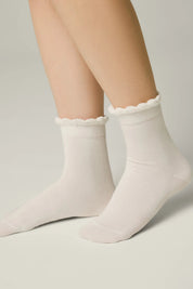 White socks with scalloped edges worn by a person on a light gray background #color_milky
