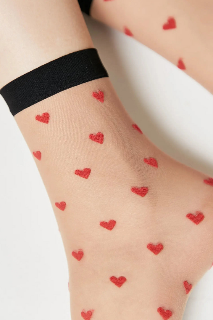 Sheer socks with red heart patterns worn by a person on a light background #color_natural-nude