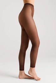 A model's legs shown from the waist down wearing sheer brown tights against a light gray studio background.