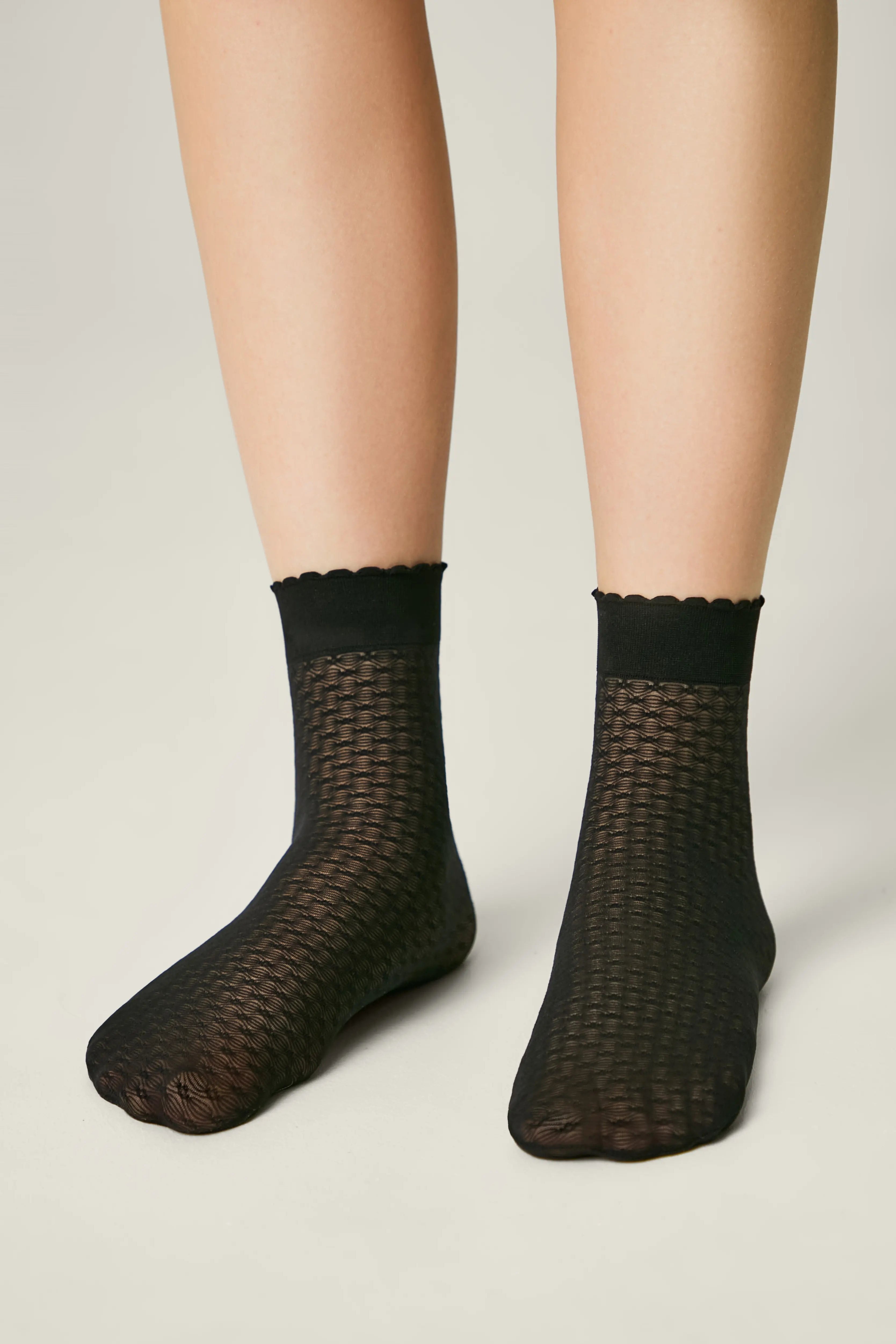 Black fishnet socks worn by a person on a light gray background #color_nero-black