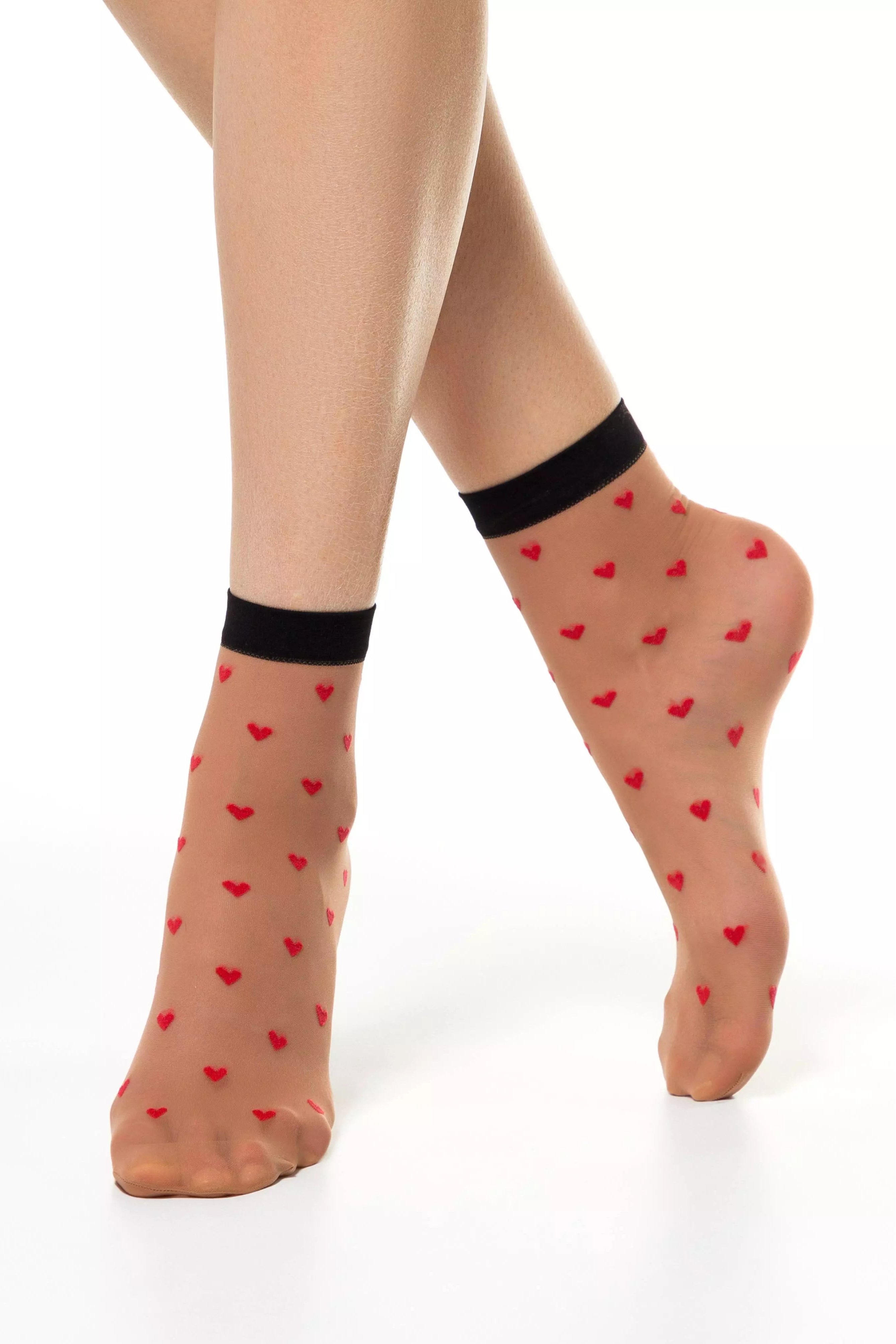 Sheer socks with red heart patterns and black cuffs worn by a person on a white background #color_natural-nude