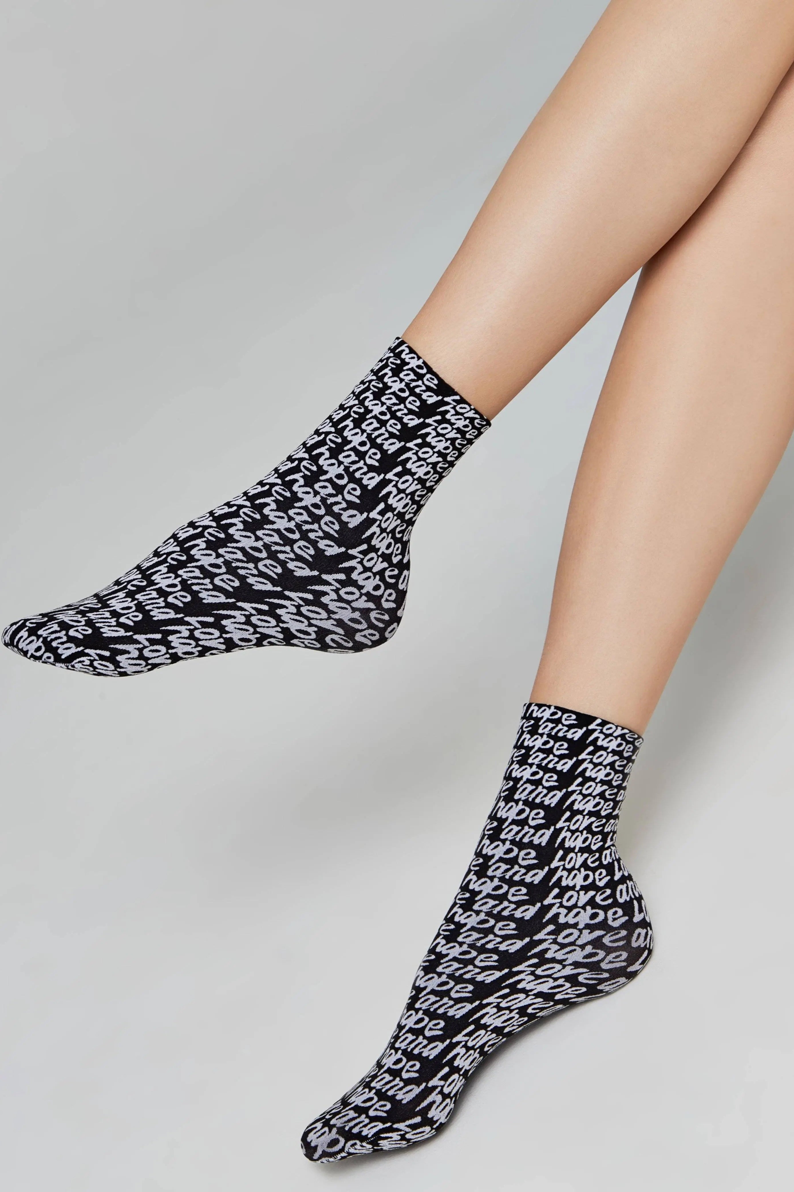 Black socks with white pattern worn by a person on a gray background #color_nero-bianco
