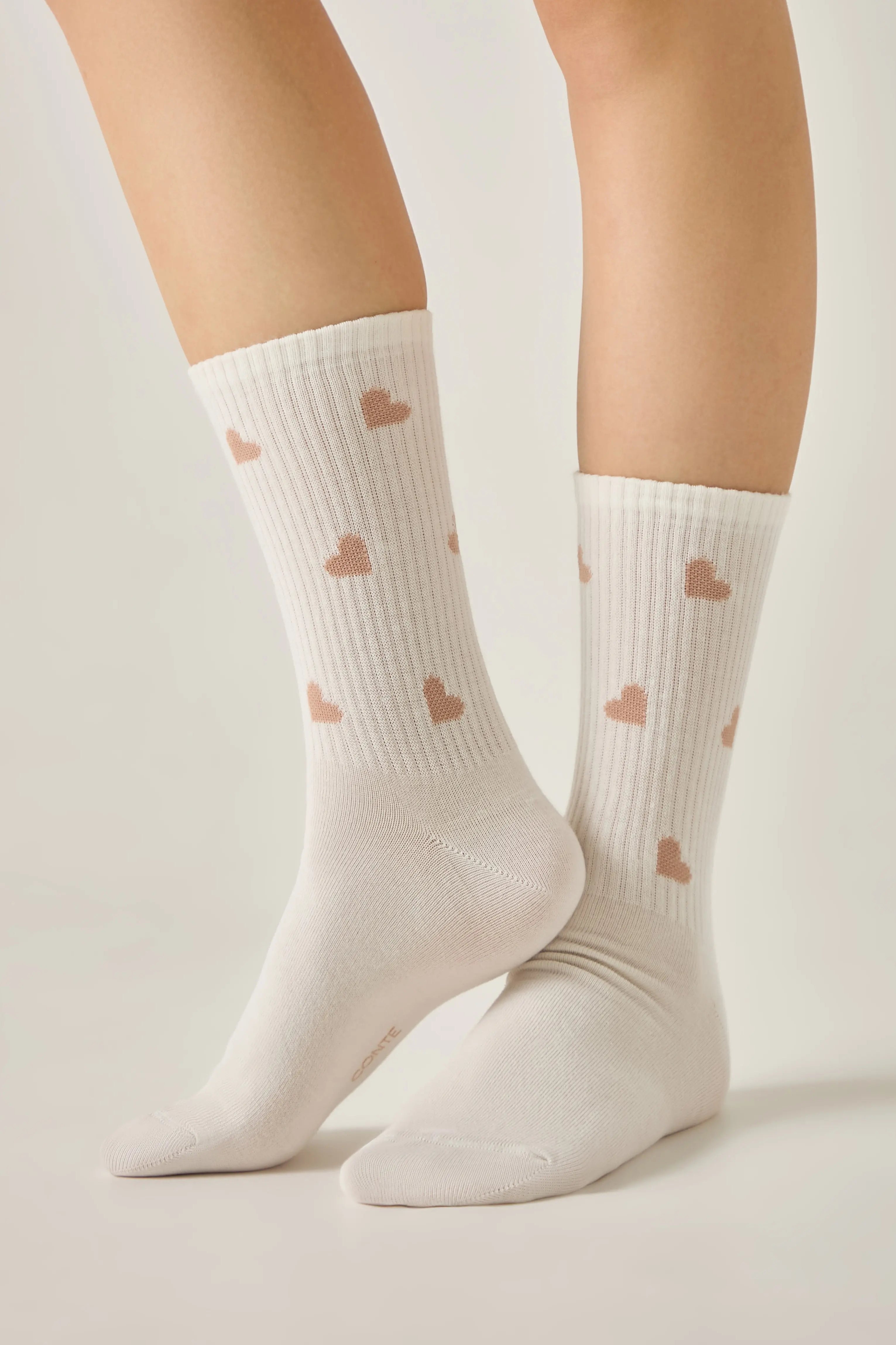 White socks with heart patterns worn by a person on a light background #color_milk