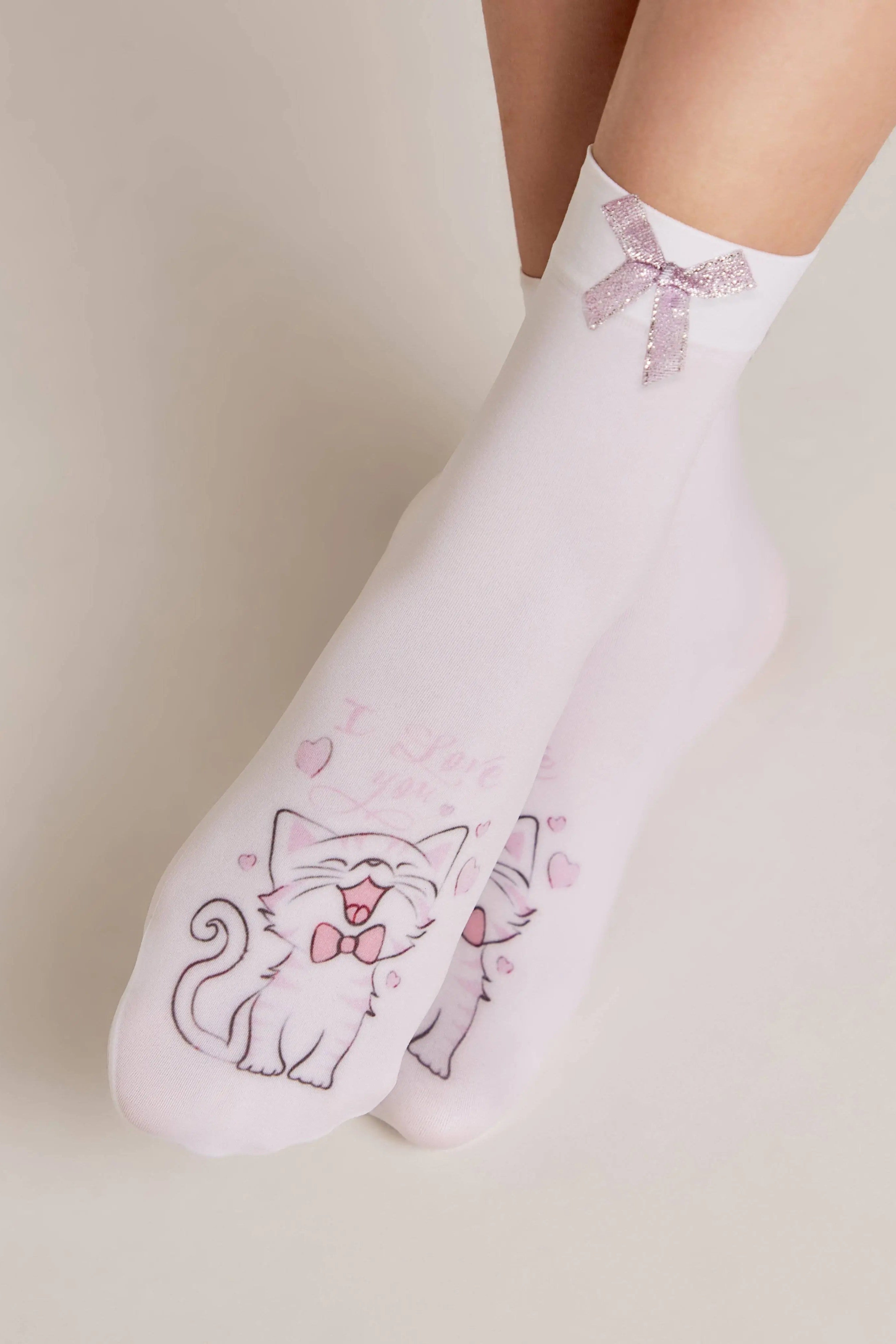 White socks with cat designs and pink bows worn by a person on a neutral background
