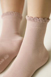 Pink socks with scalloped edges worn by a person on a light background #color_ash-pink