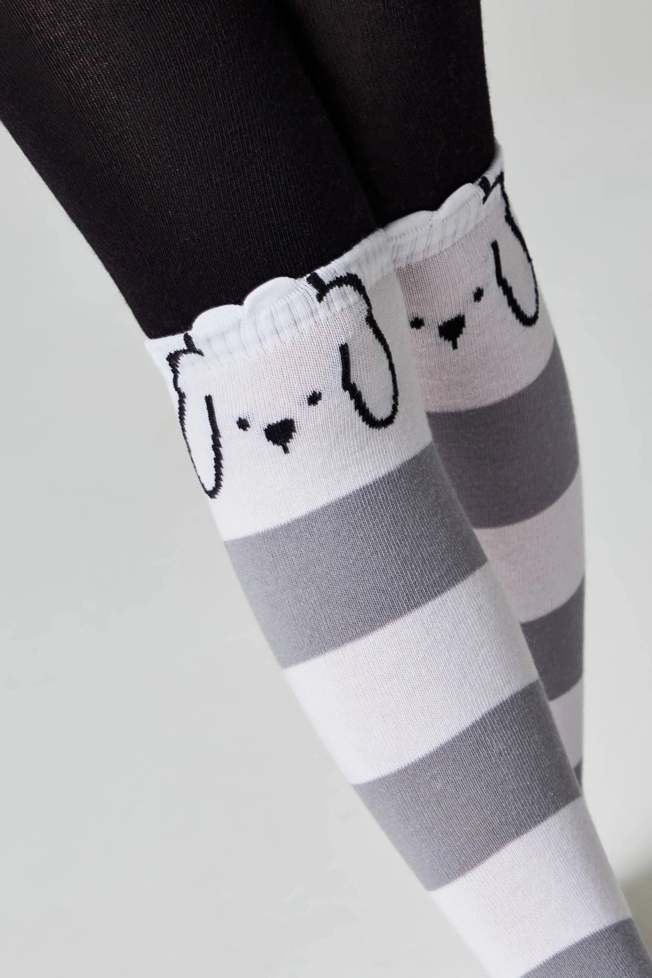 Gray and white striped knee-high socks with dog face design worn by a person.