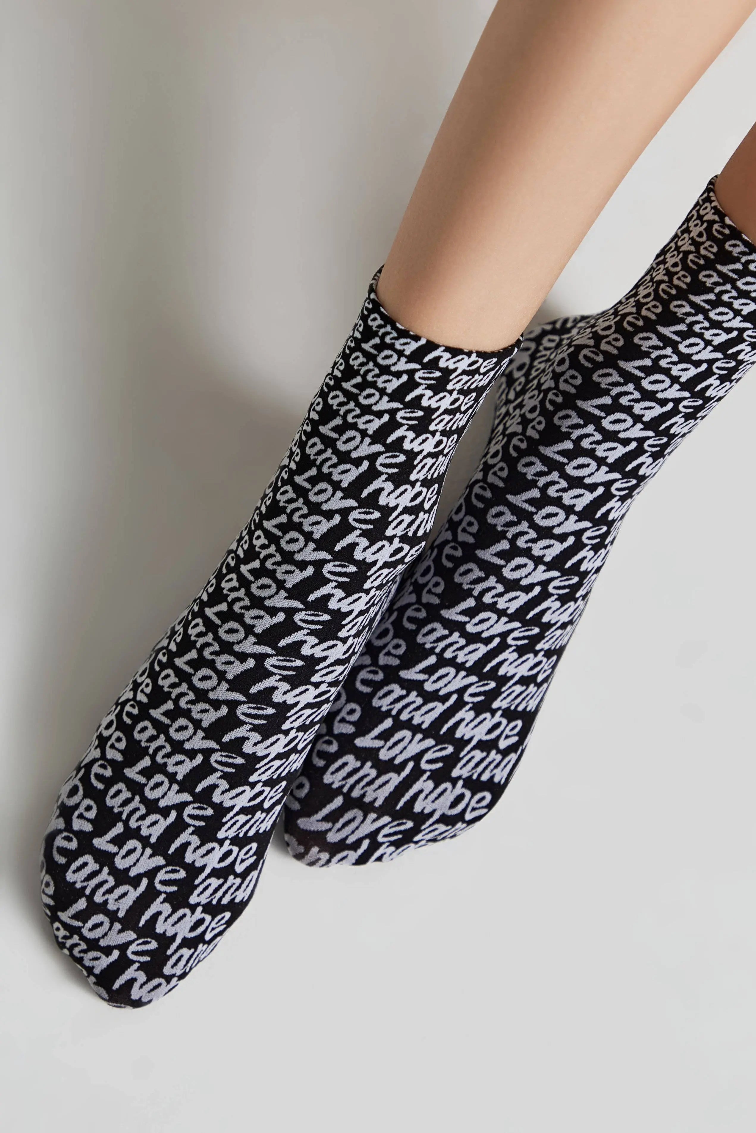 Black socks with white text worn by a person on a light gray background #color_nero-bianco