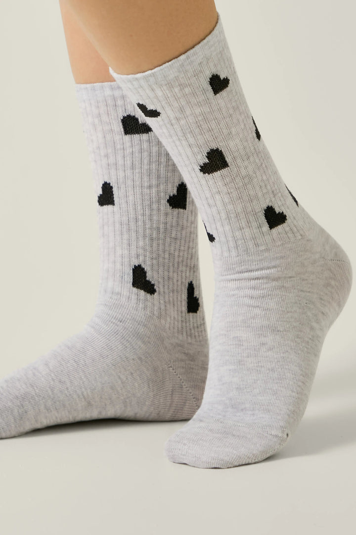 Gray socks with black heart patterns worn by a person on a light background #color_light-gray