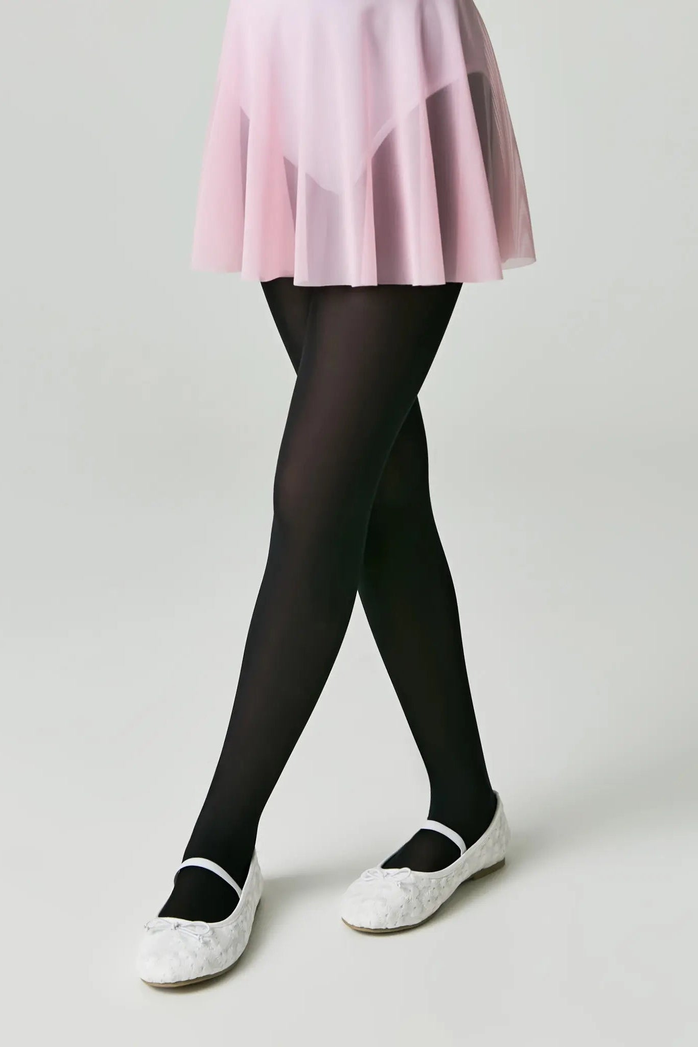 Person wearing black tights and white shoes on a plain background #color_nero-black