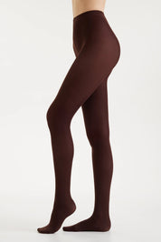 A model's legs wearing dark brown tights, shown from the waist down in a side profile against a clean white studio background.