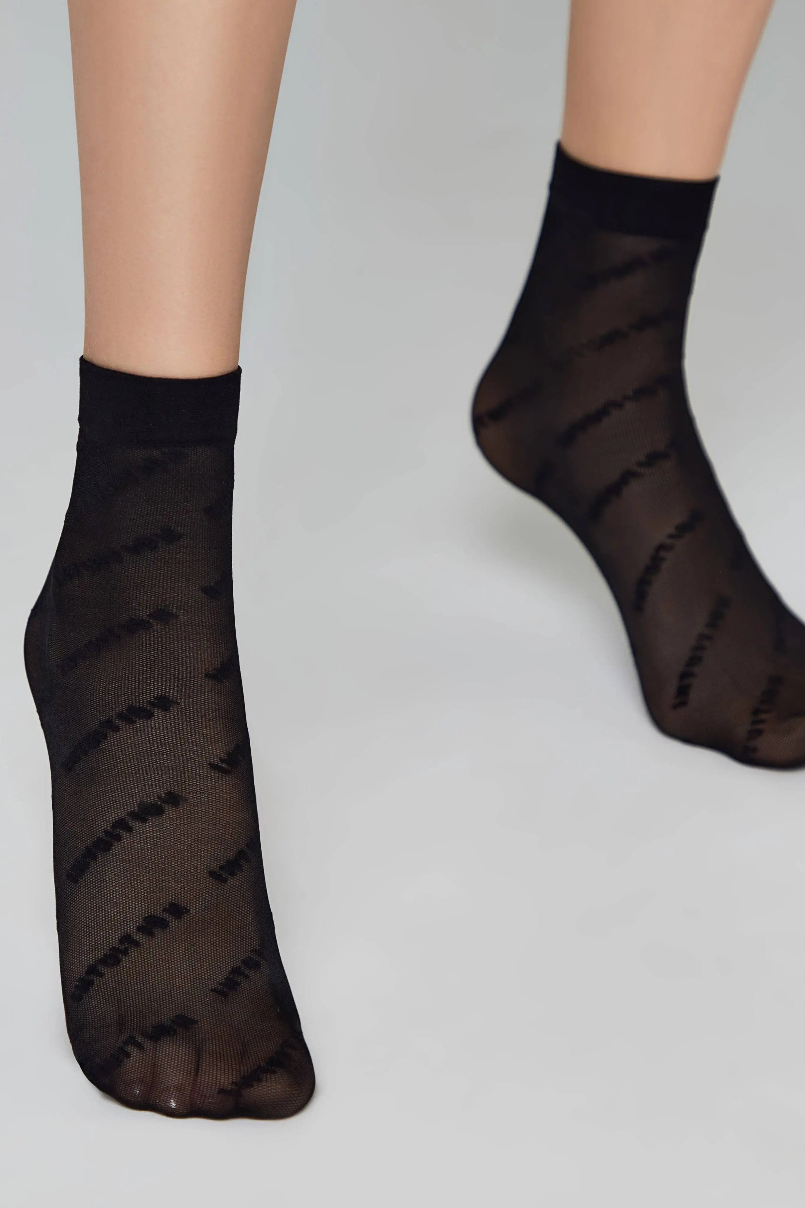 Black sheer socks with striped pattern worn by a person on a light gray background