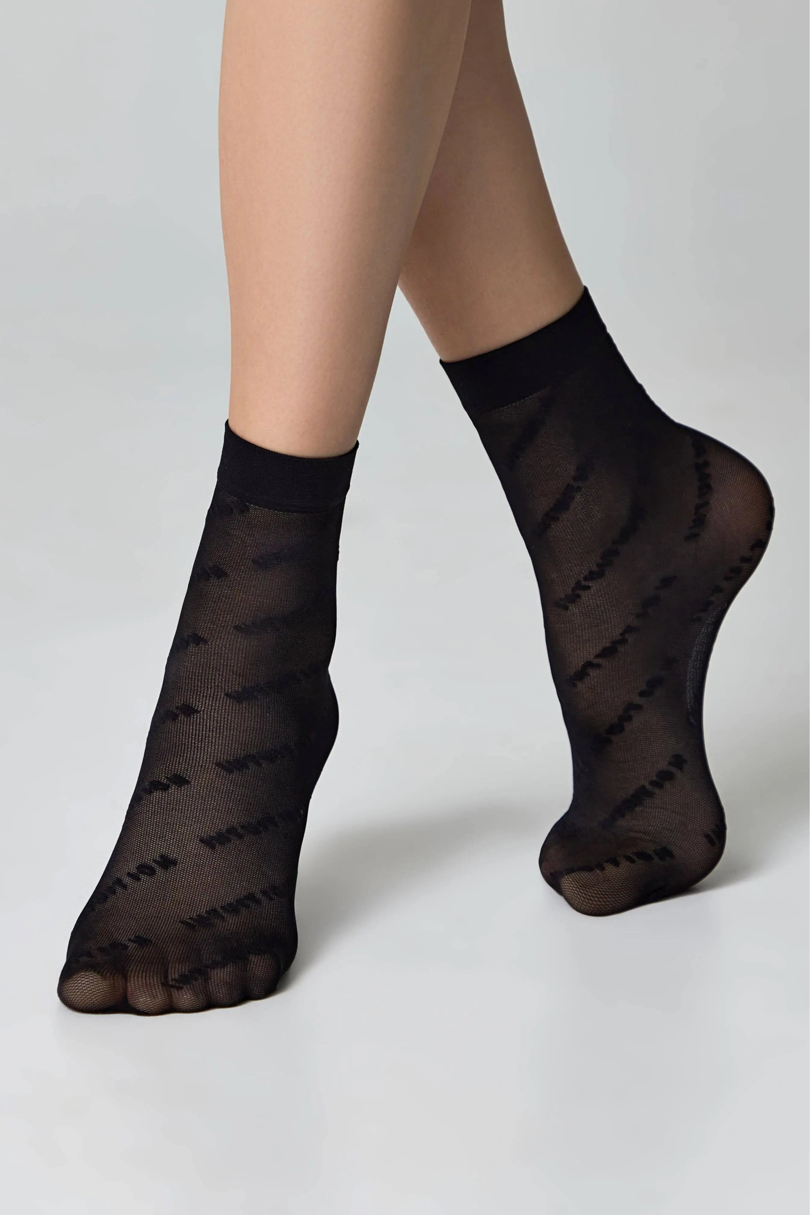 Black sheer socks with pattern worn by a person on a light gray background