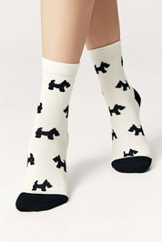 White socks with black dog pattern worn by a person on a light gray background #color_milk