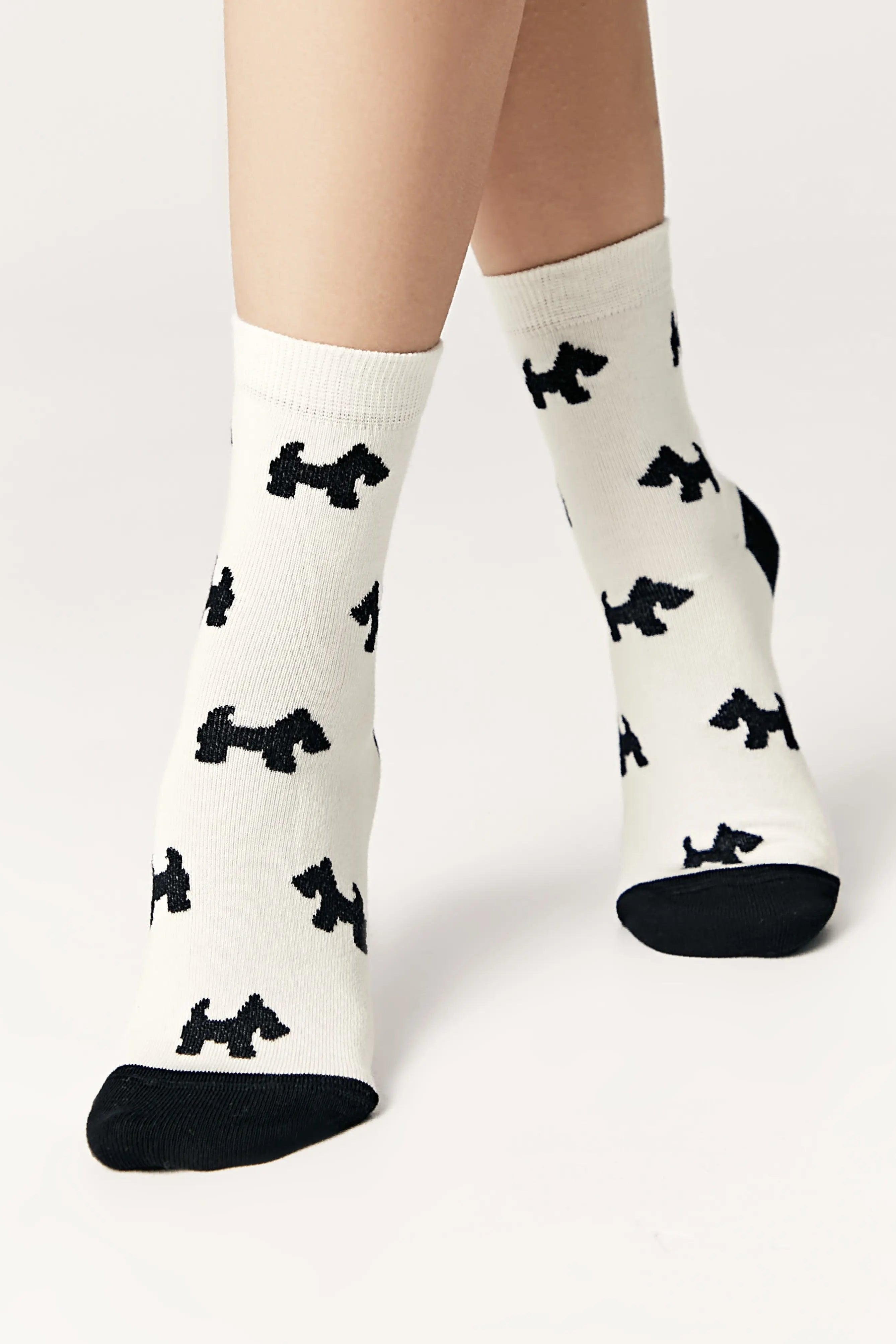 White socks with black dog pattern worn by a person on a light gray background #color_milk