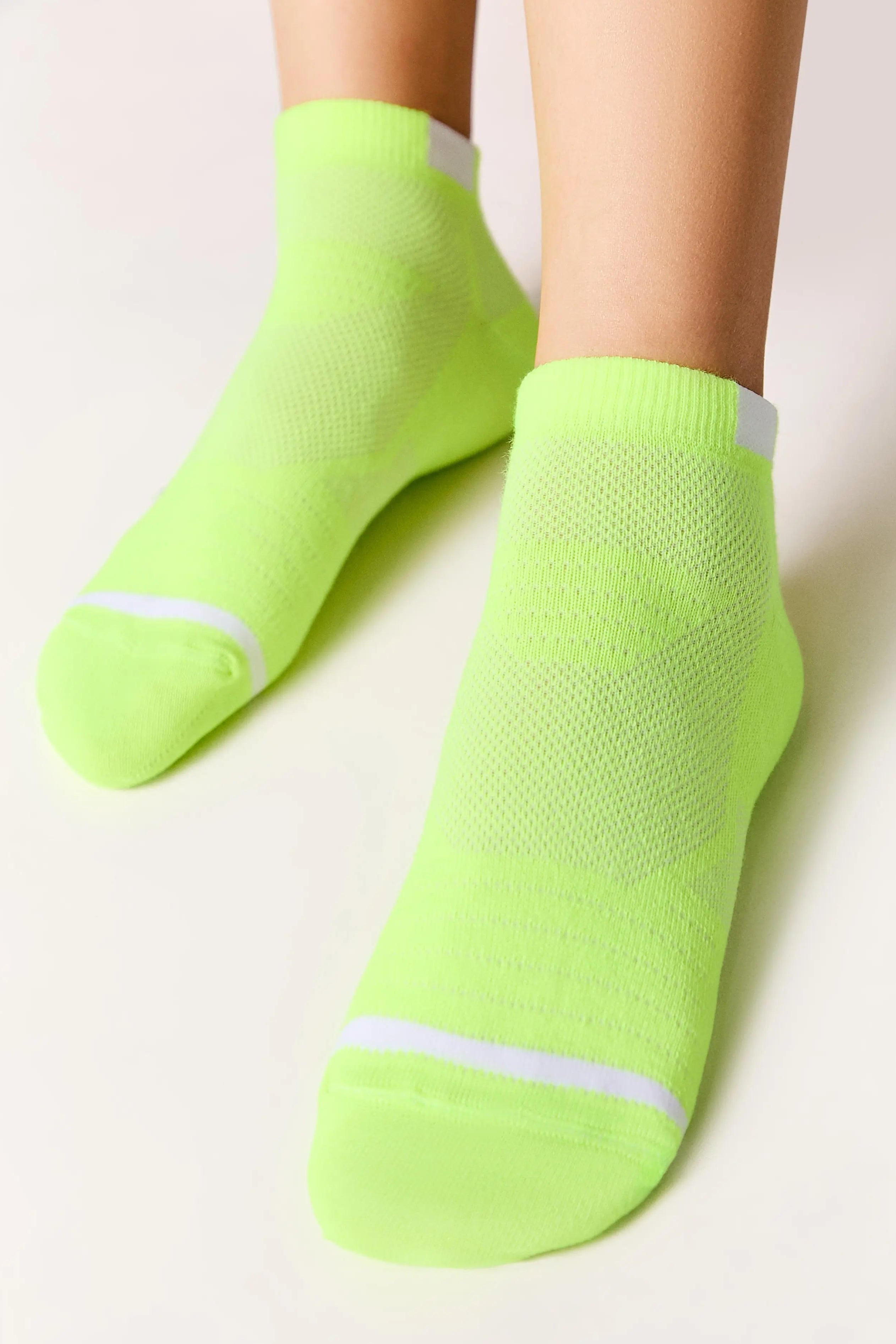 Neon green socks with white stripes worn by a person on a light background #color_lime-green