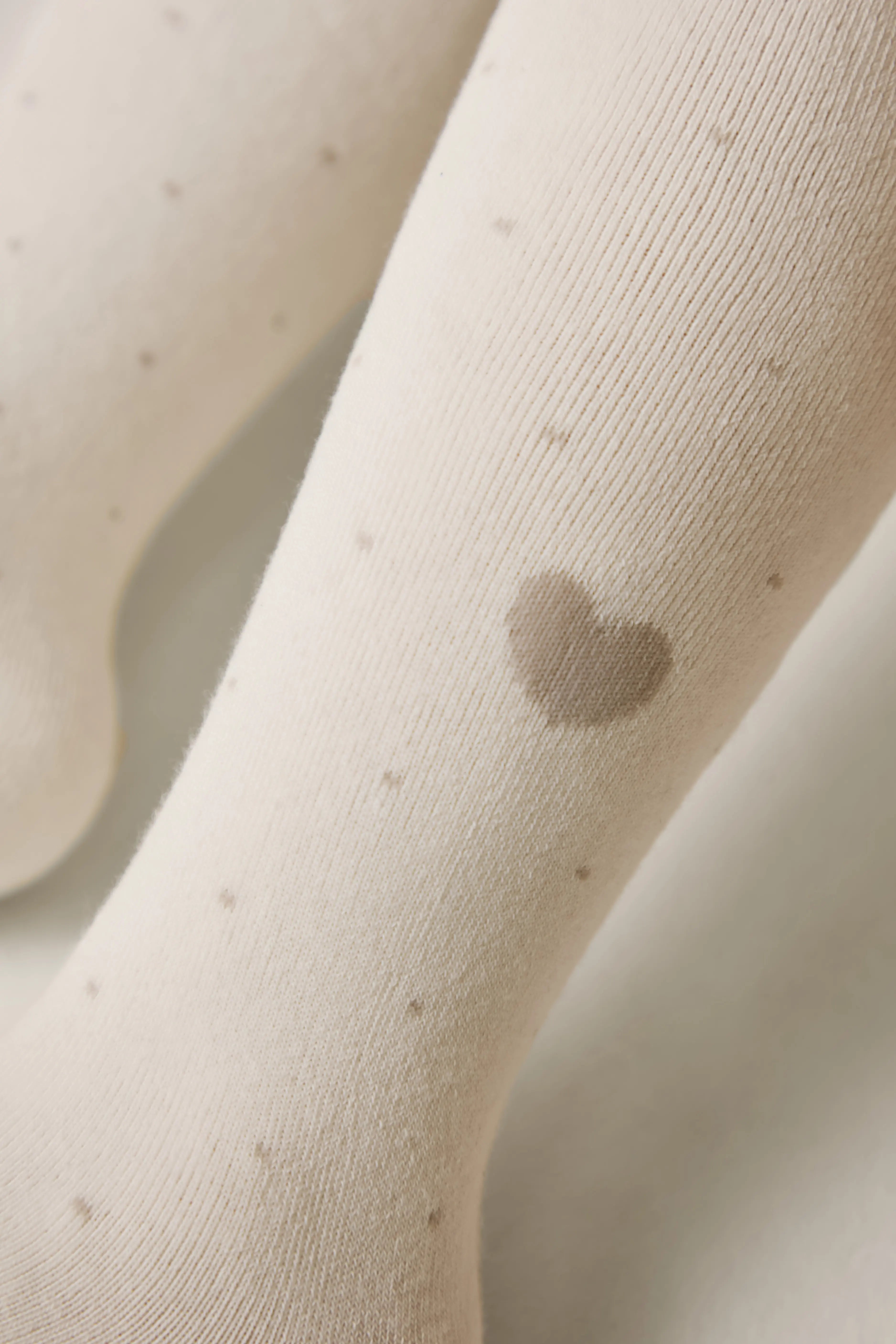 Close-up of beige tights with a heart-shaped spot on a neutral background #color_milky