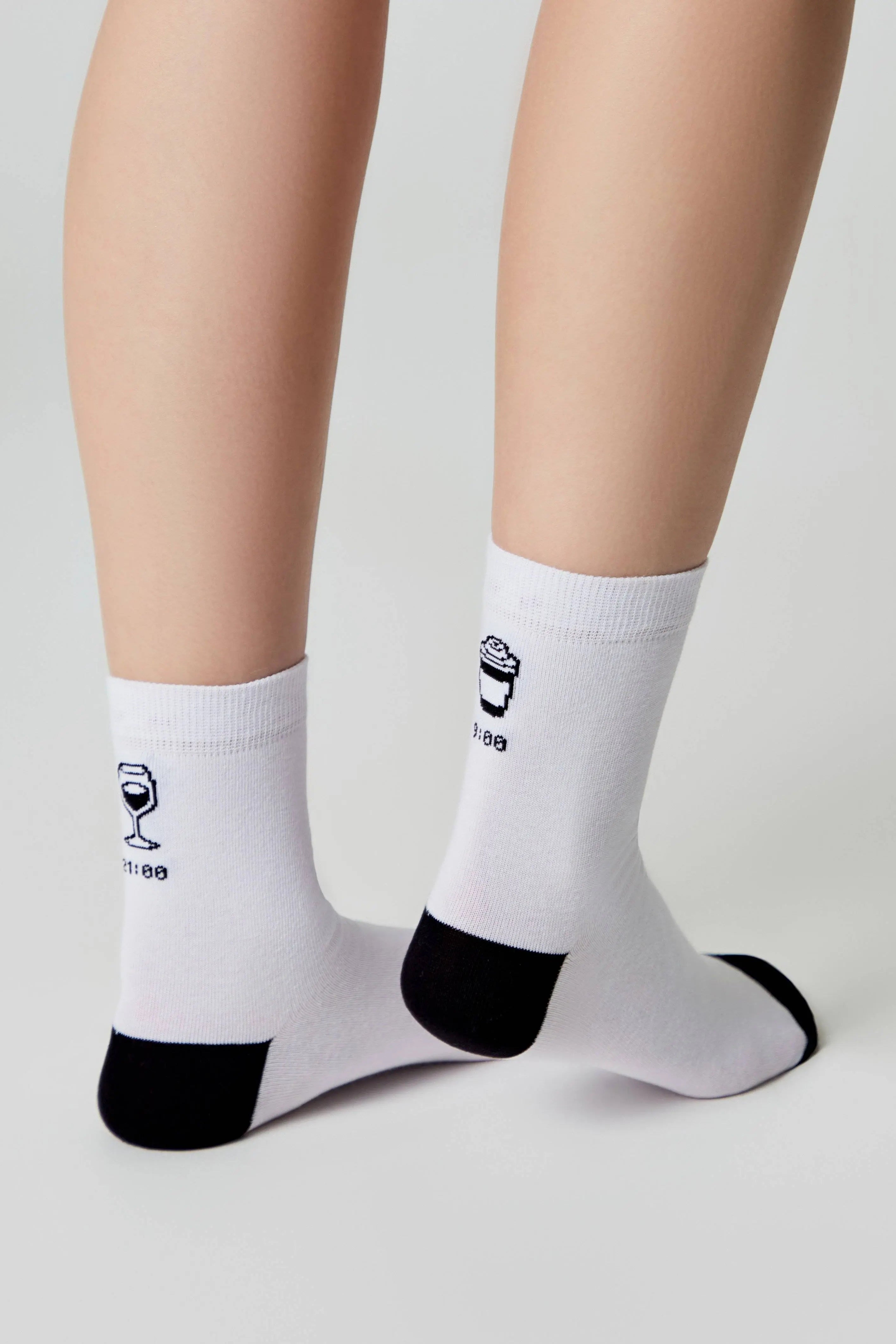 White socks with black accents and wine glass design worn by a person on a light gray background