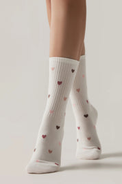 White socks with heart patterns worn by a person on a light background #color_milky