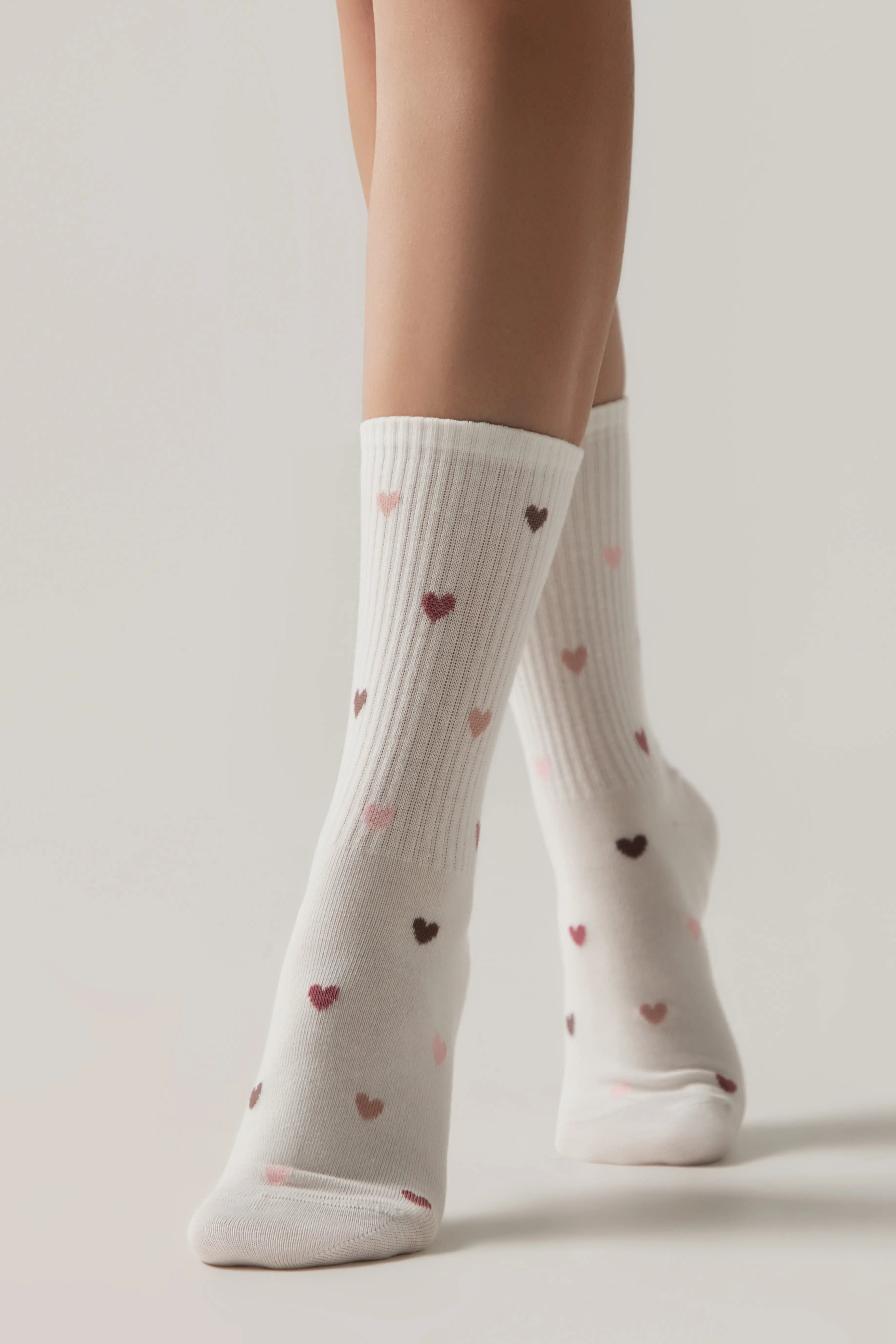 White socks with heart patterns worn by a person on a light background #color_milky