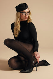 Woman wearing a black outfit with fishnet stockings and high heels on a beige background
