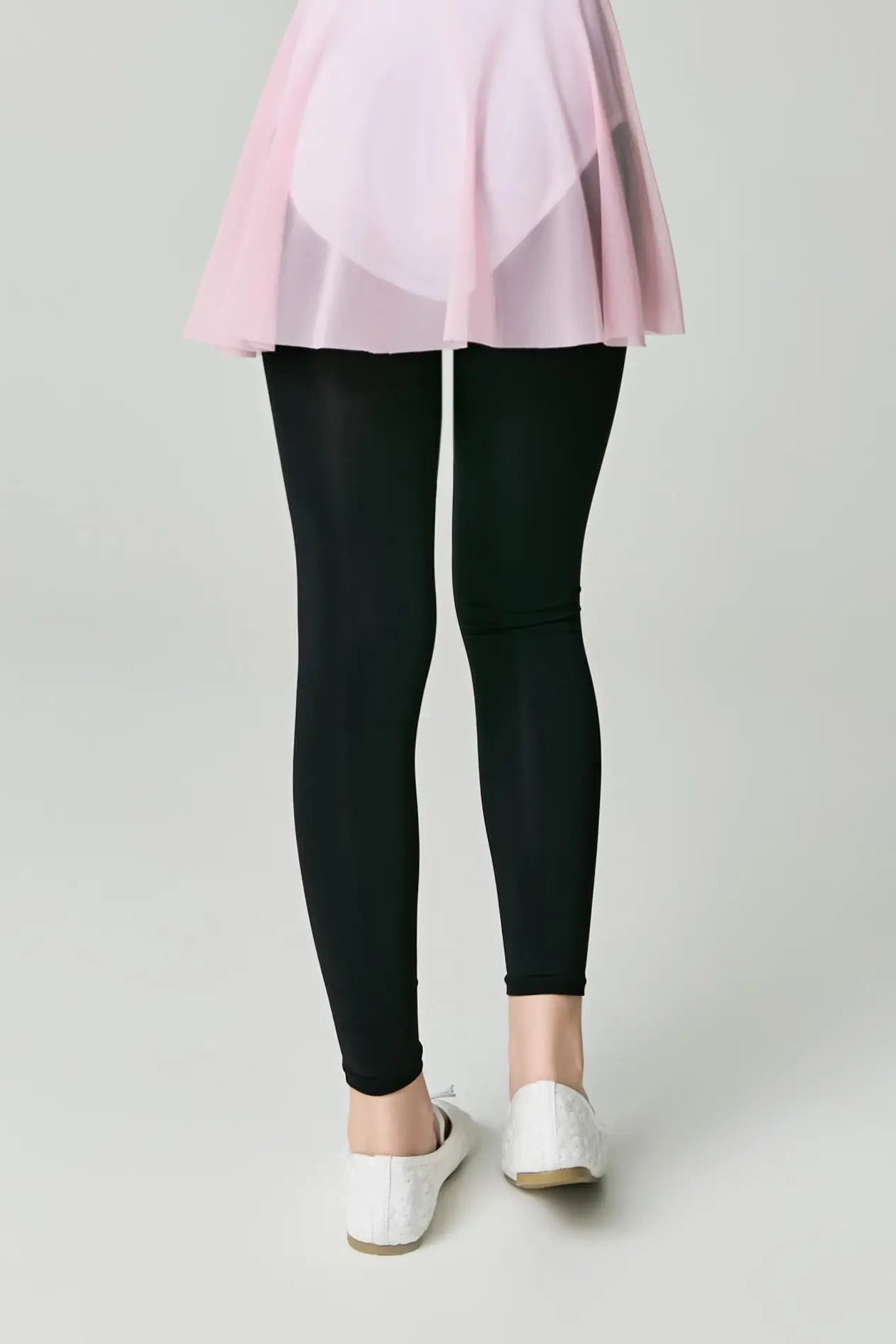 Person wearing black leggings with a light pink top and white shoes on a plain background #color_nero-black