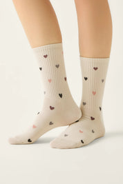 Beige socks with heart patterns worn by a person on a light gray background #color_beige